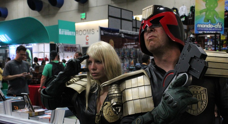 man dressed as Judge Dredd with a blonde woman saluting behind him dressed as Anderson, at San Diego ComicCon
