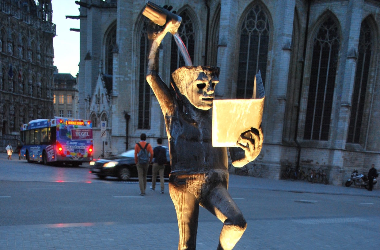 [IMAGE] A bizarre statue featuring a mythical creature reading a book while pouring a glass of liquid into its head. In the background is a large church.