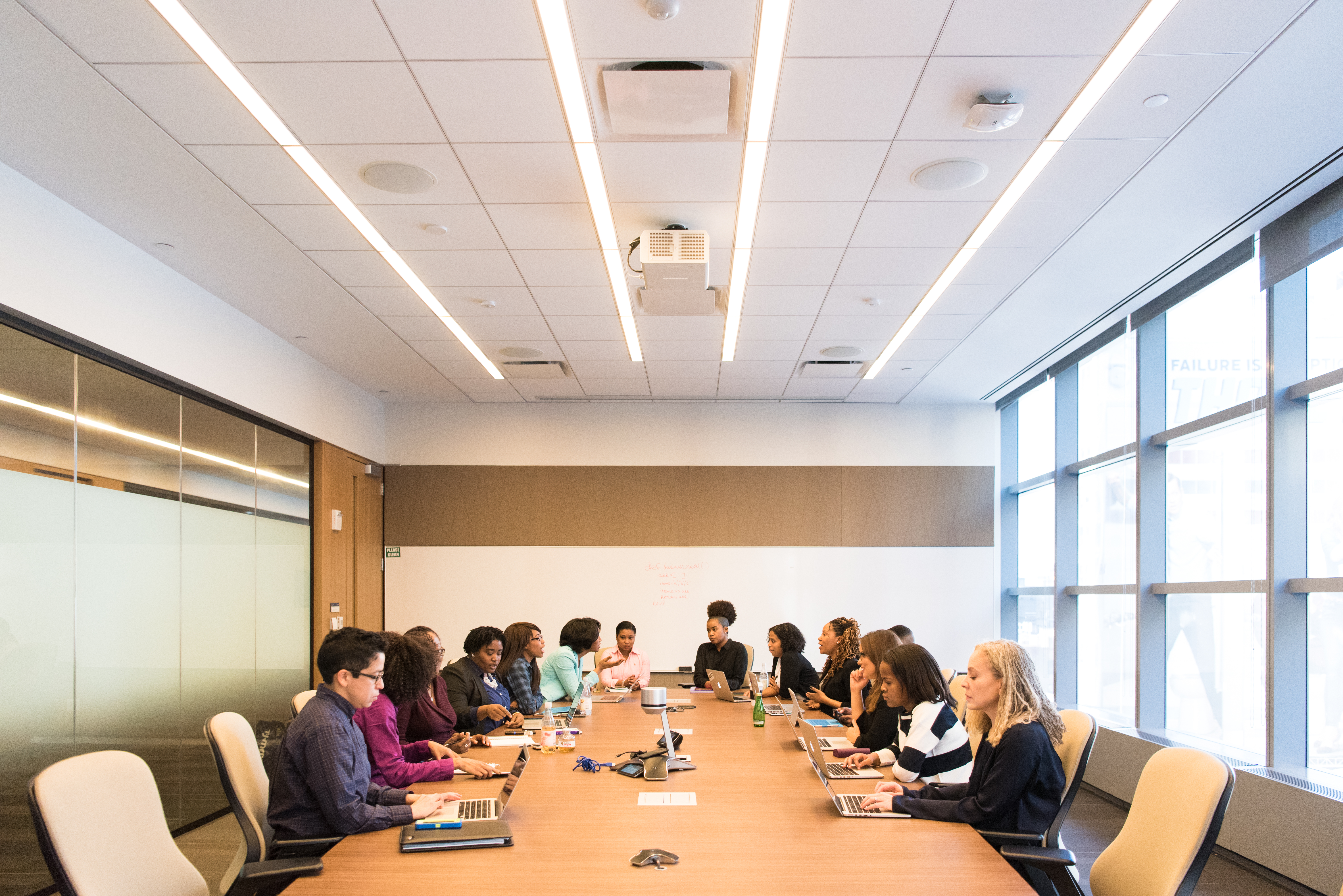 [IMAGE] A group of mostly female-presenting people of color with open laptops sitting around a meeting table